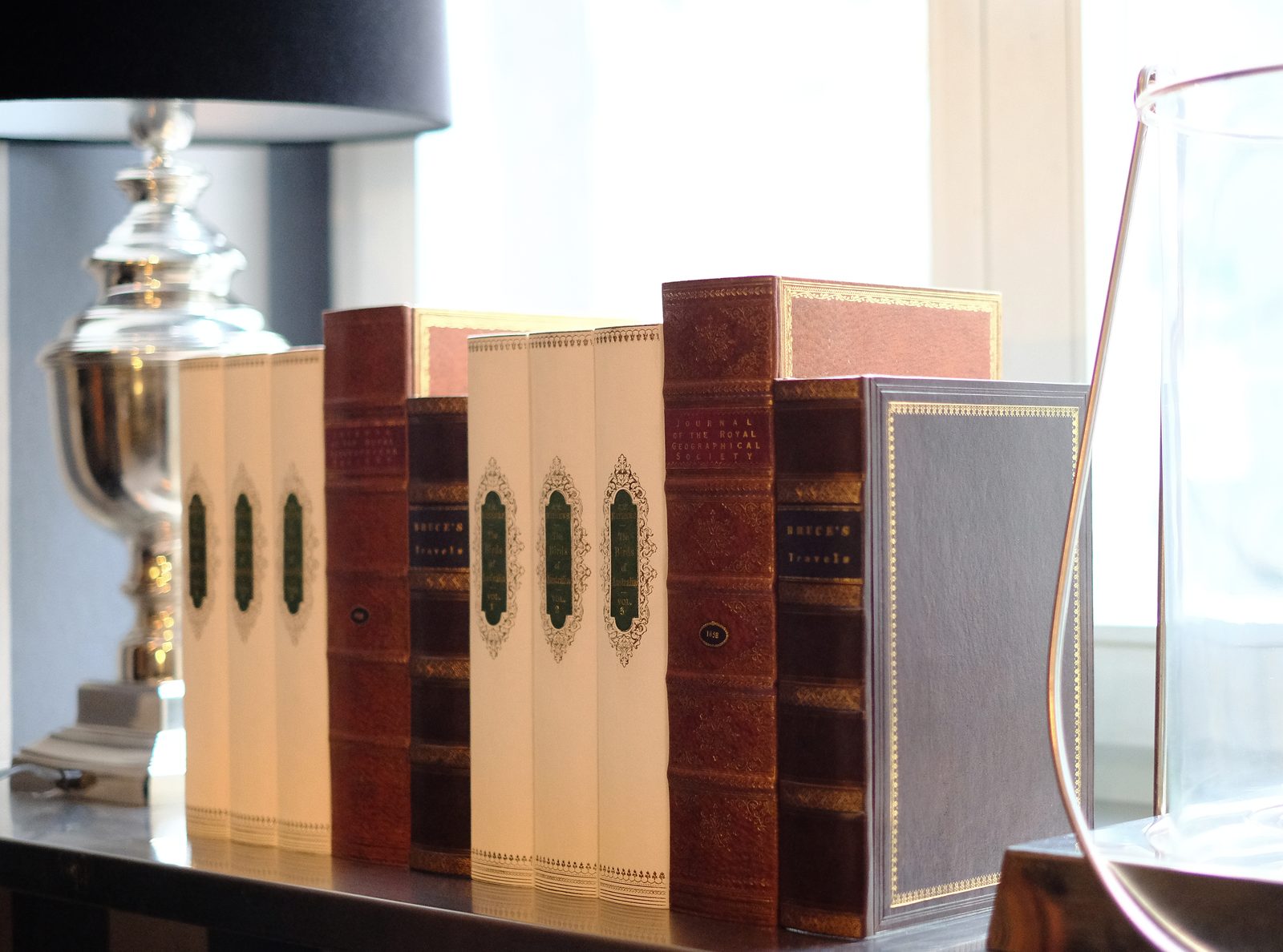 Book spine wall art: leather-bound book spines styled on a shelf beside a lamp